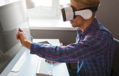 Man in VR goggles touching computer monitor